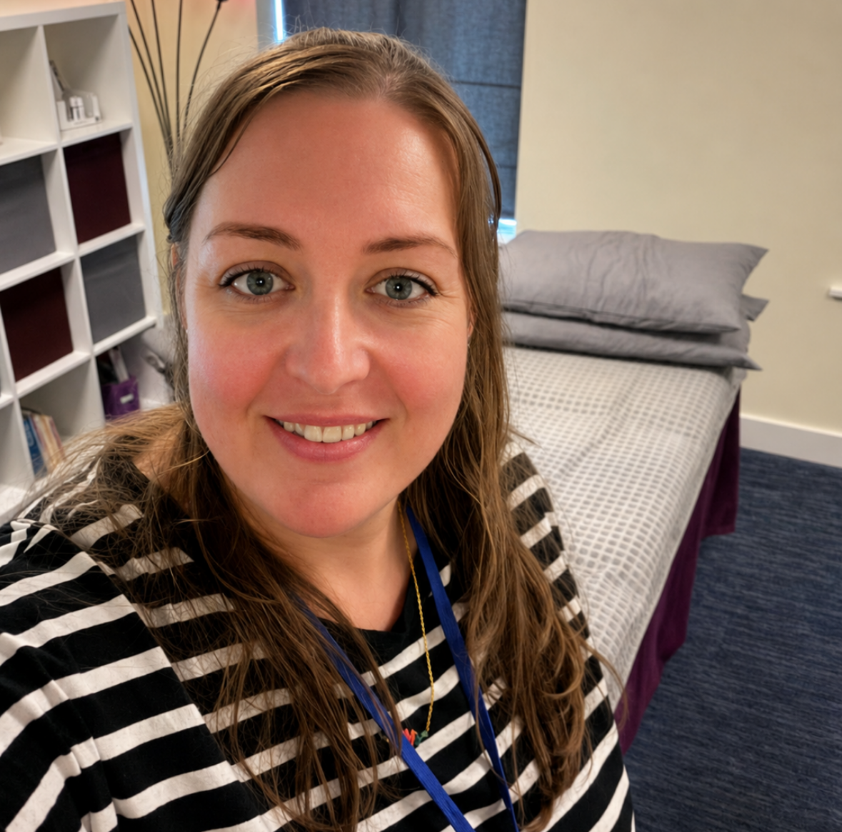 Woman smiling in a treatment room beside a bed and storage shelves