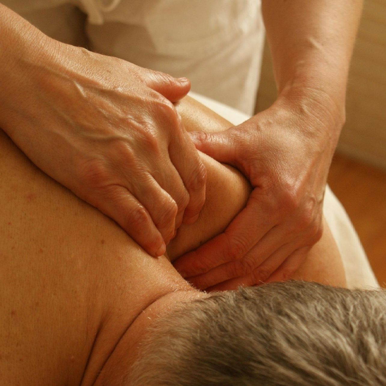 Hands massaging a person's shoulder and upper back. Focus on the hands pressing into the skin.