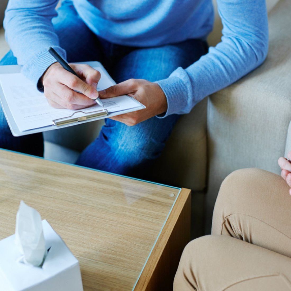 Therapist taking notes during a counseling session. A tissue box is on the table.