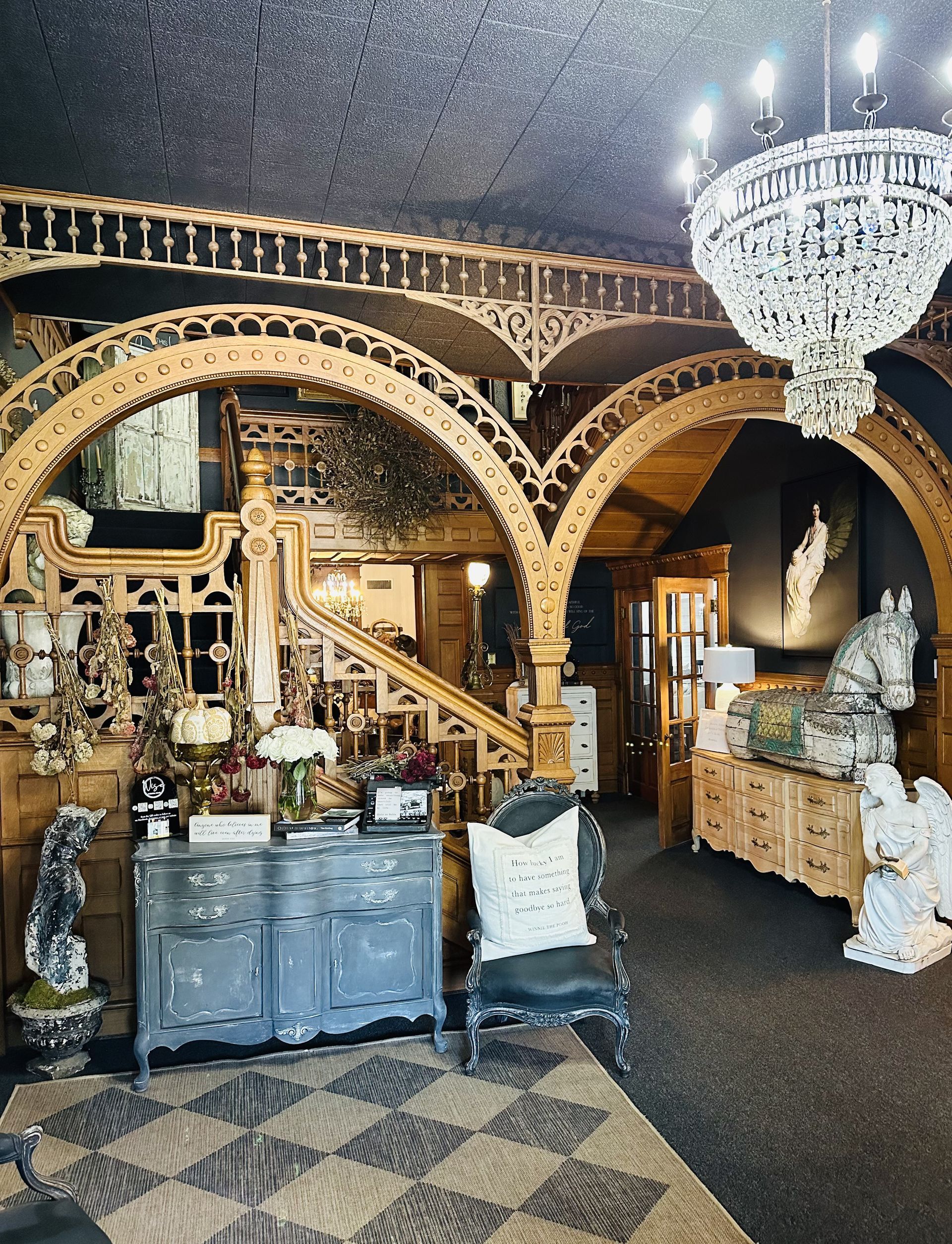 Ornate interior with arched wooden details, chandelier, decorative furniture, and a horse statue.