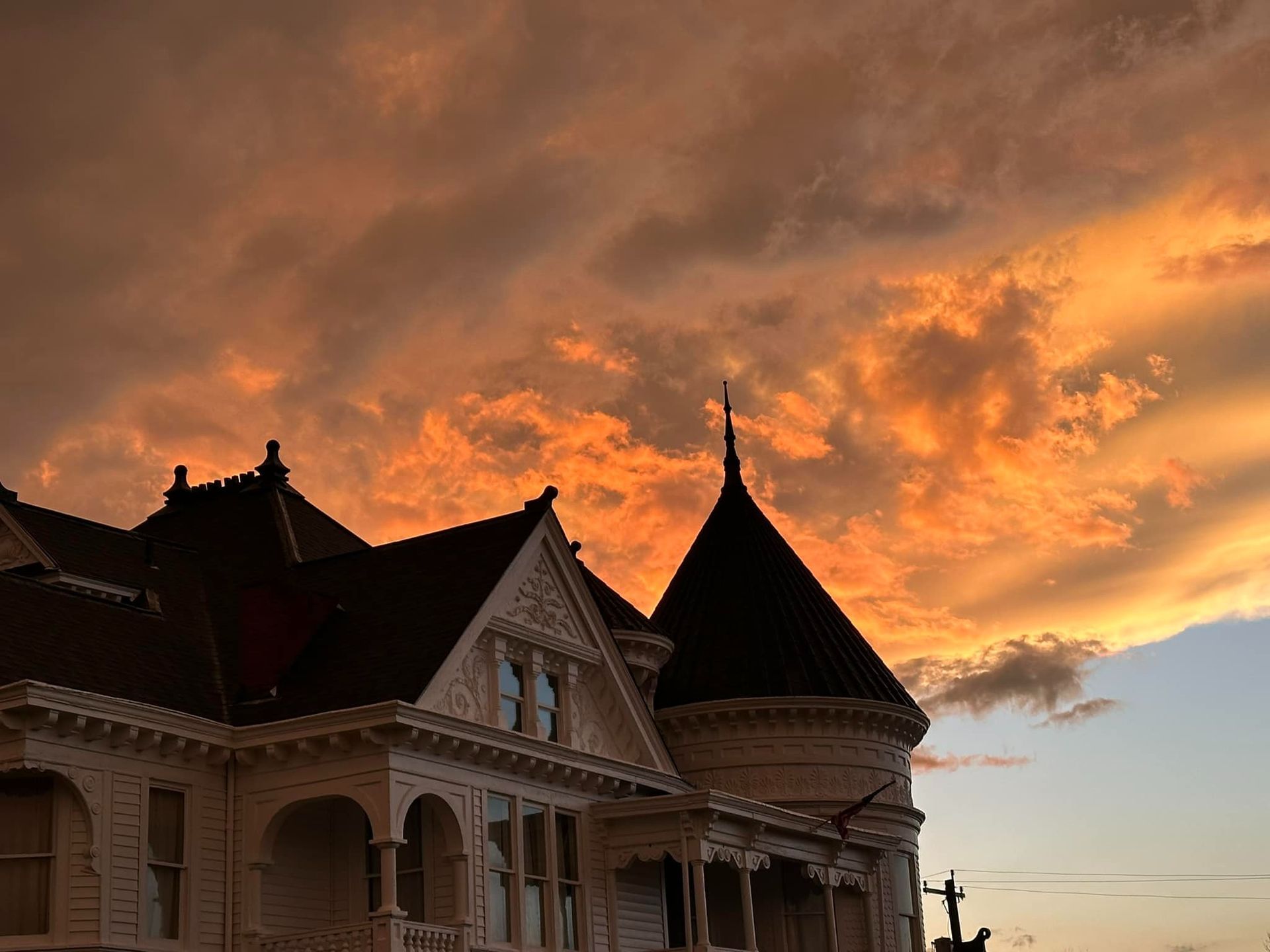 Victorian house silhouetted against a fiery orange and yellow sunset sky.