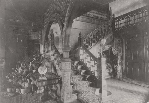 Ornate staircase in a Victorian-era house, with detailed carvings and potted plants.