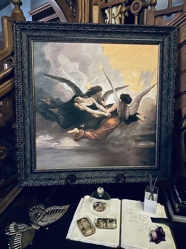 Painting of angels in a stormy sky, framed on a desk with inkwell, letters and ornate objects.