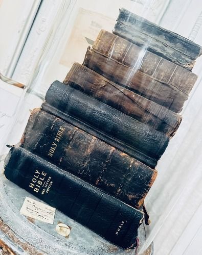 Stack of old, dark leather-bound Bibles inside a glass display case.