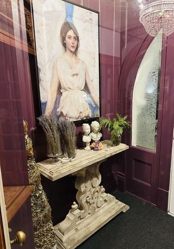 Hallway with table and artwork.  A painting of a woman, busts, and dried lavender are on a carved console table in a purple-walled room.