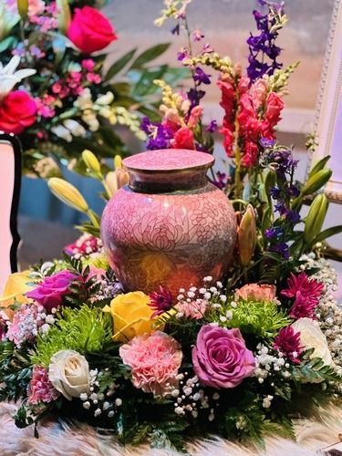 A group of people are standing around a wooden urn surrounded by red roses at a funeral.