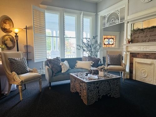 Living room with gray sofa, ornate chairs, decorative fireplace, and large windows.
