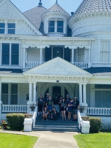 Group of people posing on the steps of a white Victorian house.