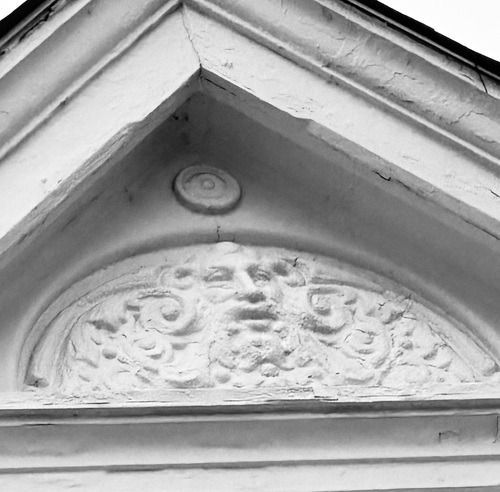 Triangular pediment with carved face and ornate scrollwork detail.