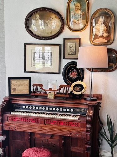 Antique organ with framed vintage portraits and a lamp.