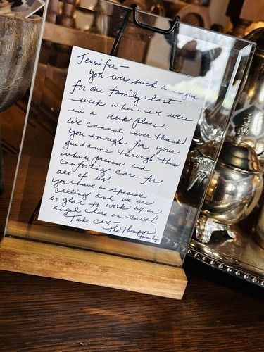 Handwritten note in a frame on a wooden base with silverware in the background.
