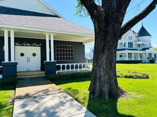 A chapel and a Victorian house on a green lawn with a tree in the foreground.