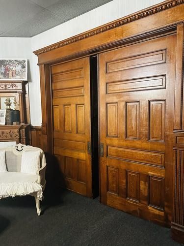 Wooden sliding doors open to reveal a dark room, ornate trim, and a small decorative table with a chair.