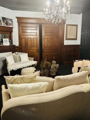 Elegant room with antique wooden doors, cream-colored sofas, and a chandelier; decorative pillows and figurines.