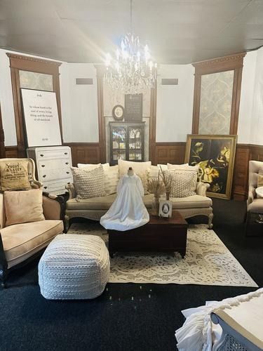 Living room with couch, coffee table, chandelier, and a wedding dress on display.