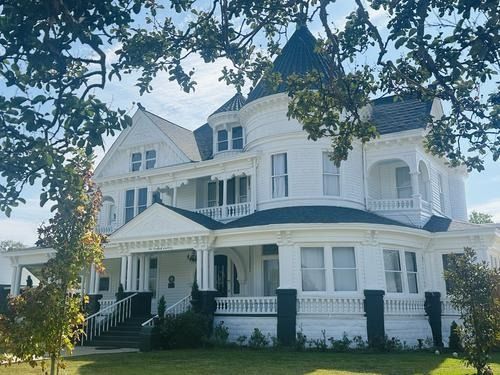 White Victorian house with a dark turret, framed by tree branches.