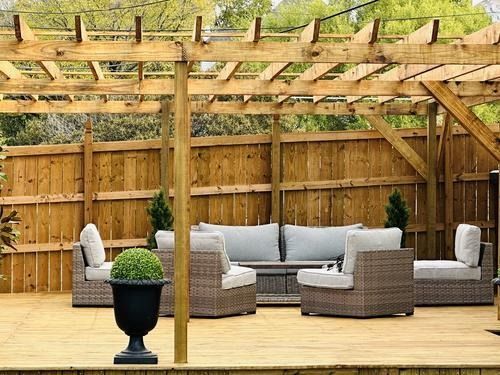 Outdoor patio with wooden pergola, seating, and hedge in decorative pot.