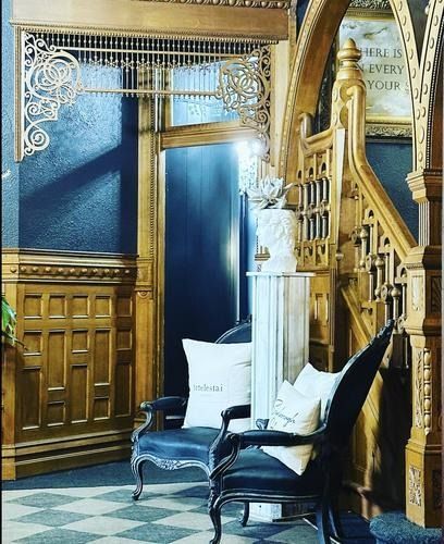 Ornate wooden interior with chairs, marble column, dark blue walls, and a staircase.