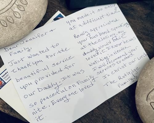 Handwritten thank you note on a wooden surface, with two stones. Note is addressed to 