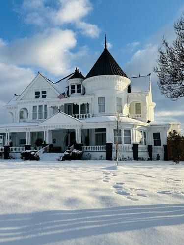White Victorian house with a black turret, covered in snow, under a blue sky.