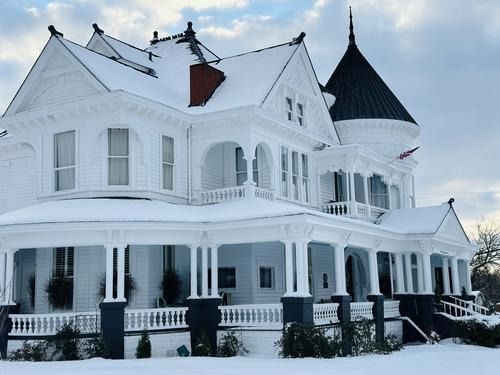 White Victorian house covered in snow, with a tower and wraparound porch.