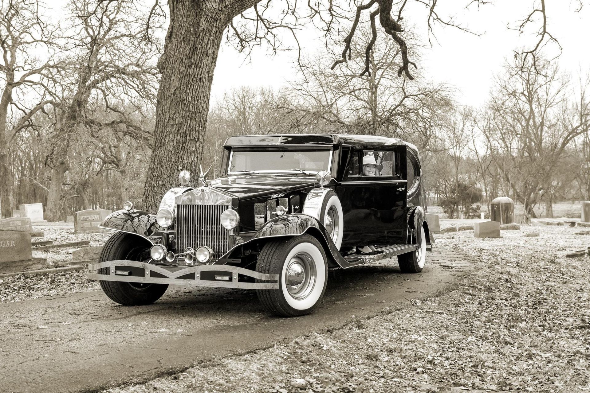 Black vintage car parked on a path in a cemetery, sepia tone.