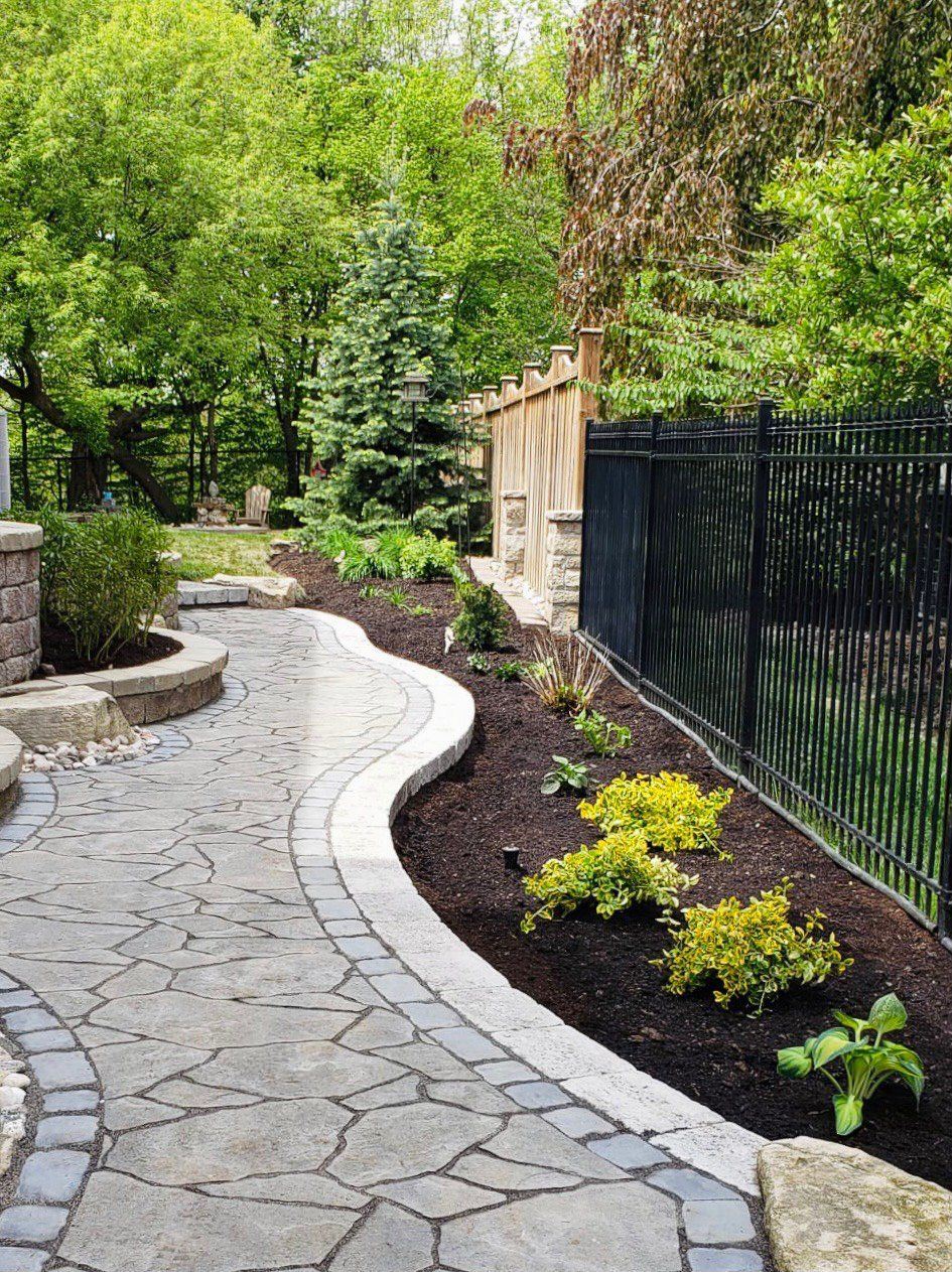 A stone walkway leading to a fence in a backyard surrounded by trees.