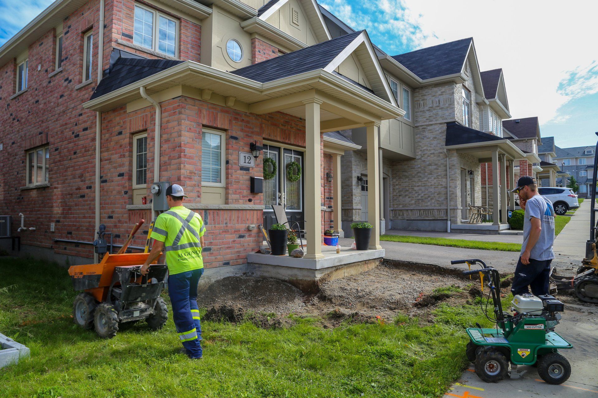 A man is standing in front of a brick house with a lawn mower.