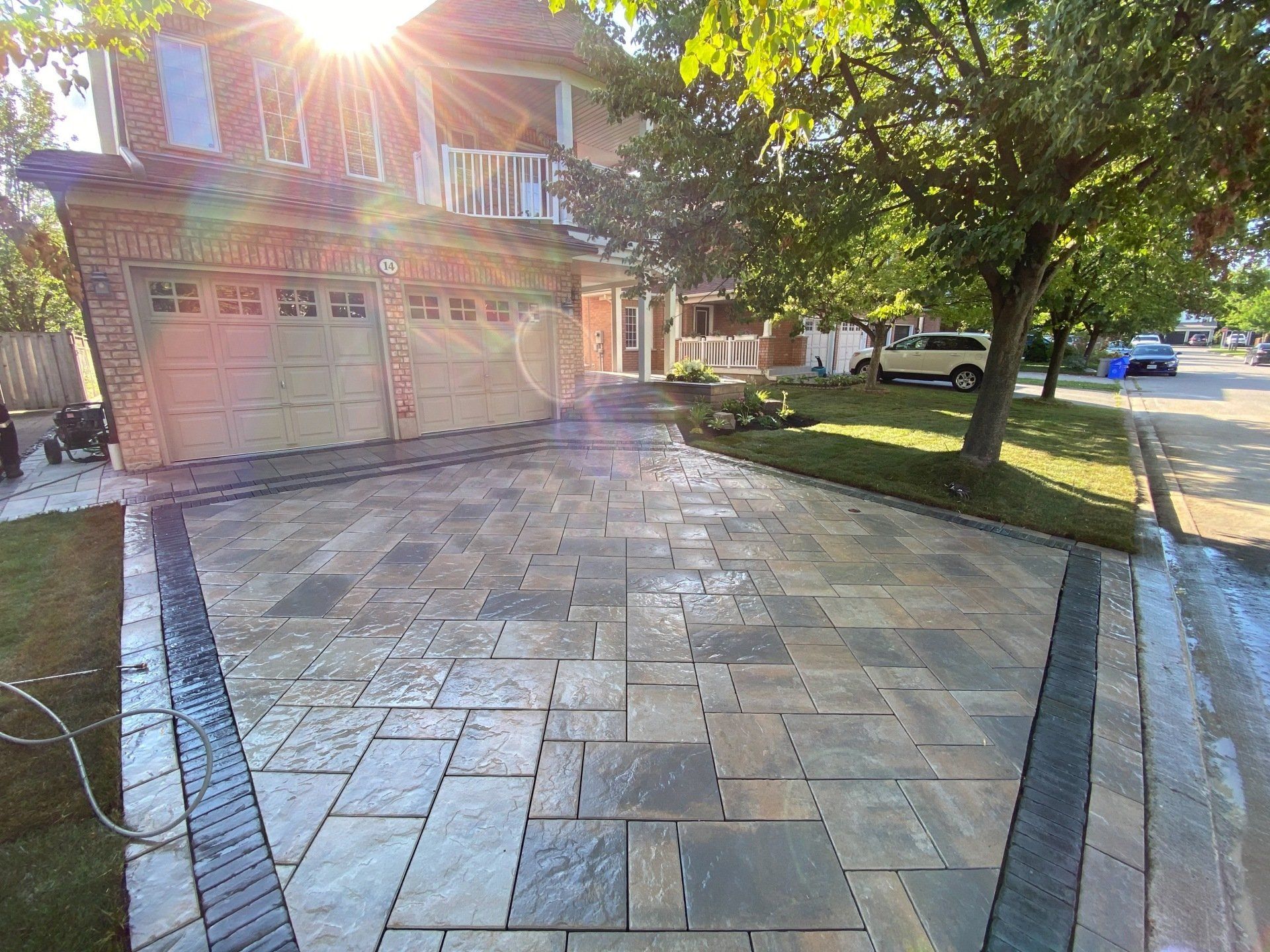A driveway in front of a house with the sun shining through the trees.
