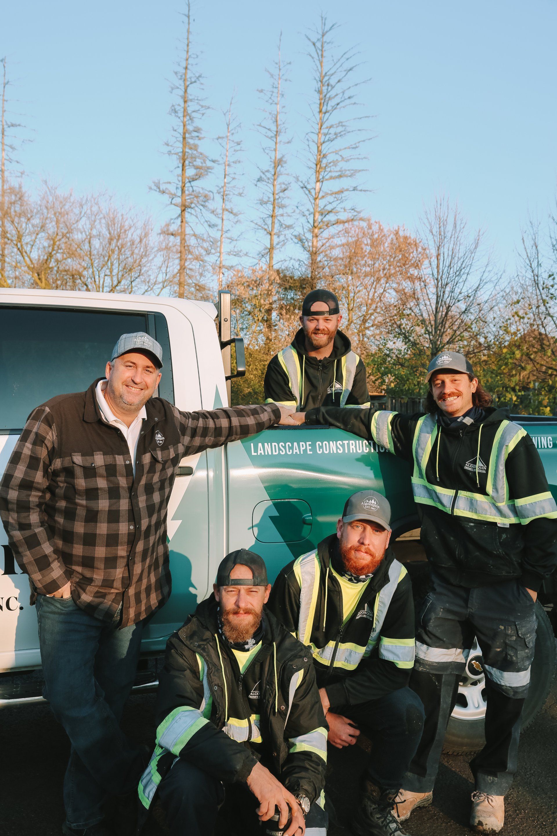 A group of construction workers are posing for a picture in front of a truck.
