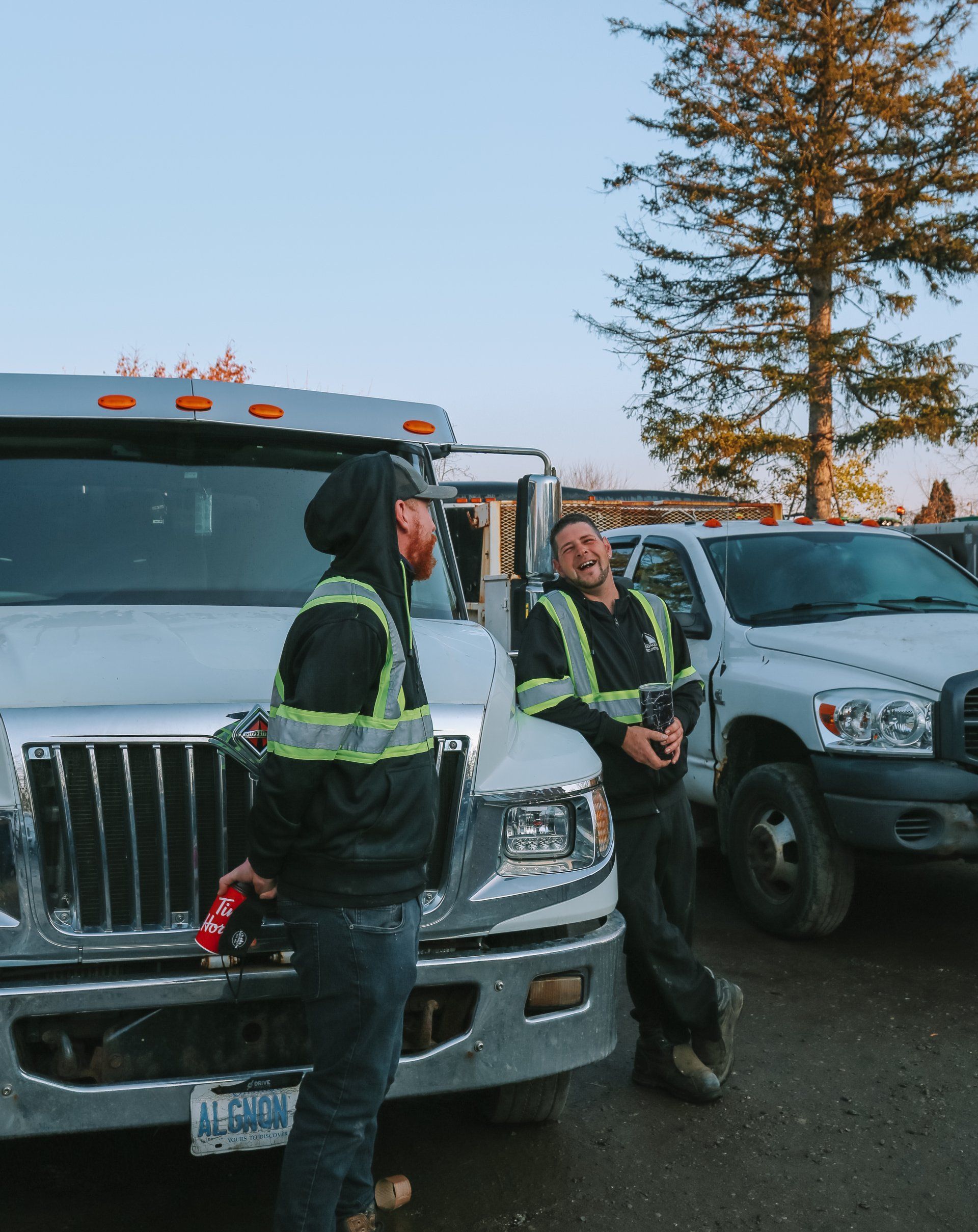 Two men in safety vests are standing in front of trucks