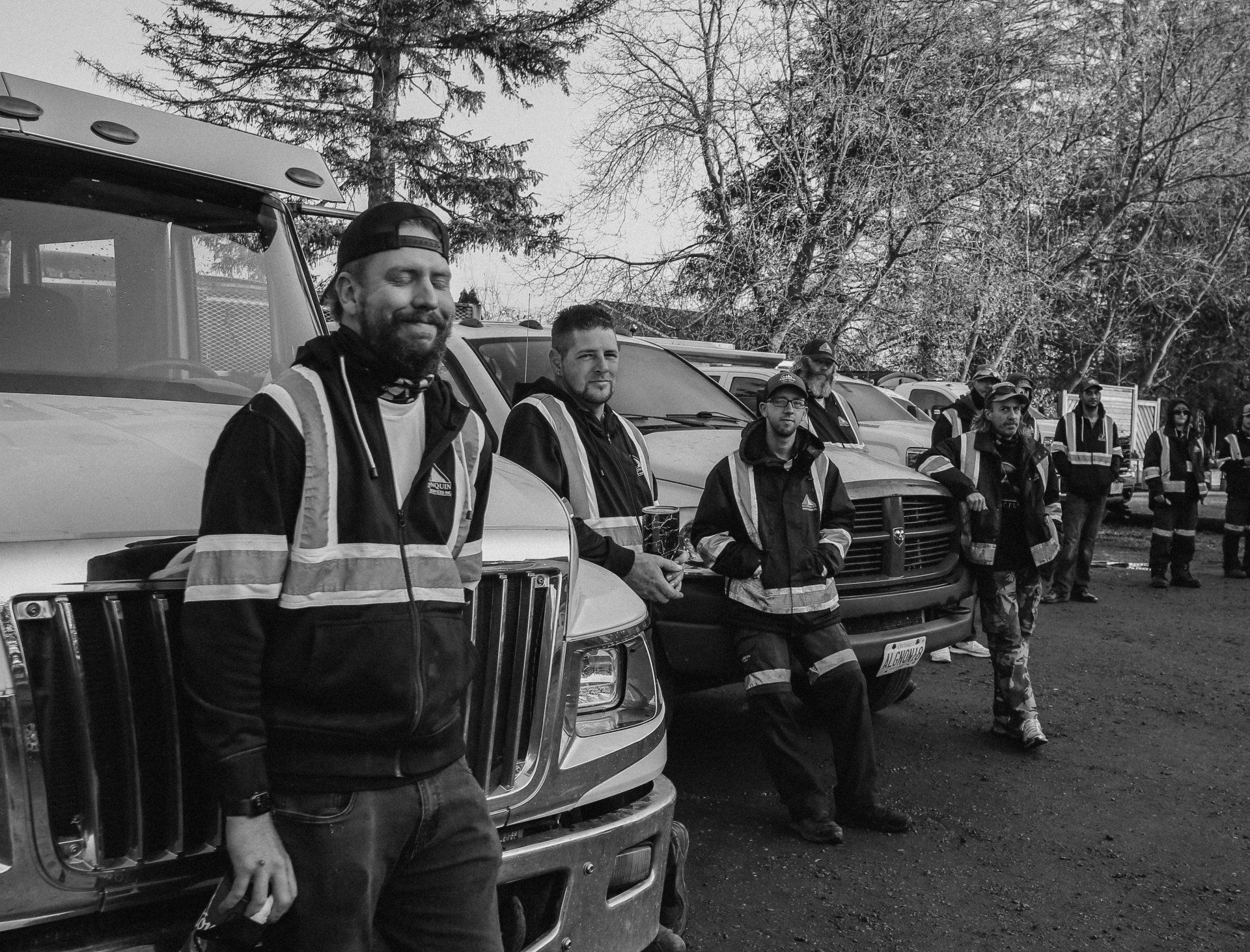 A group of men are standing next to trucks in a parking lot.