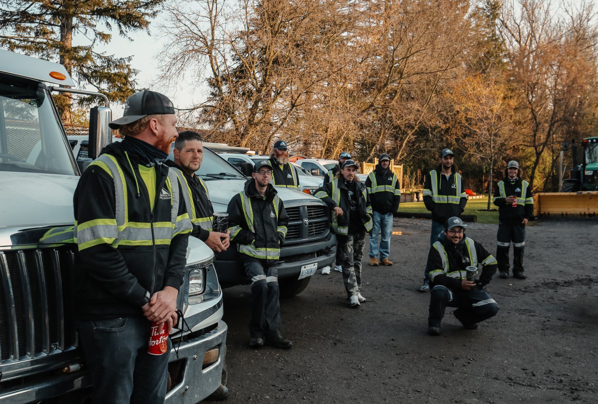 A group of construction workers are standing next to trucks in a parking lot.