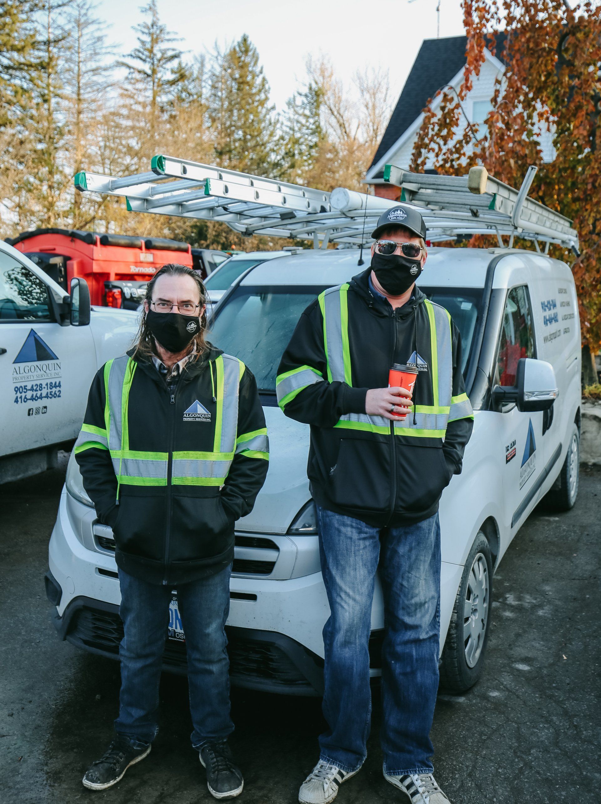 Two men wearing masks are standing in front of a van.