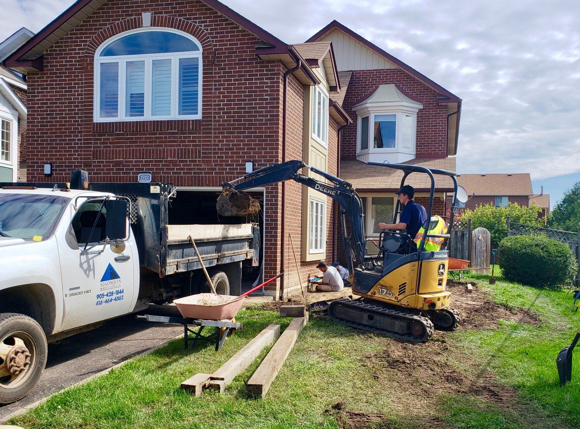 A man is driving a small excavator in front of a brick house.