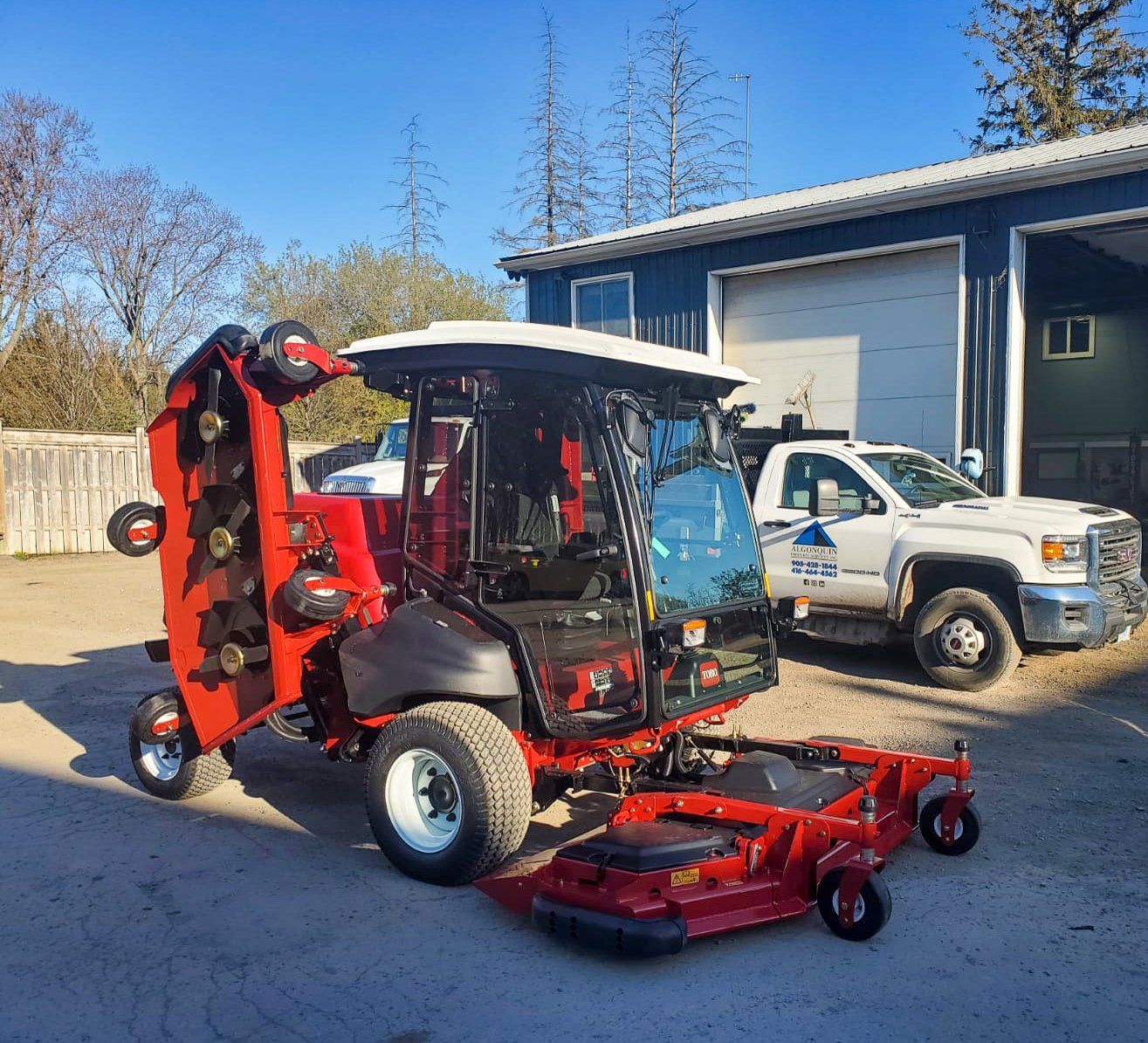 A red lawn mower is parked next to a white truck.