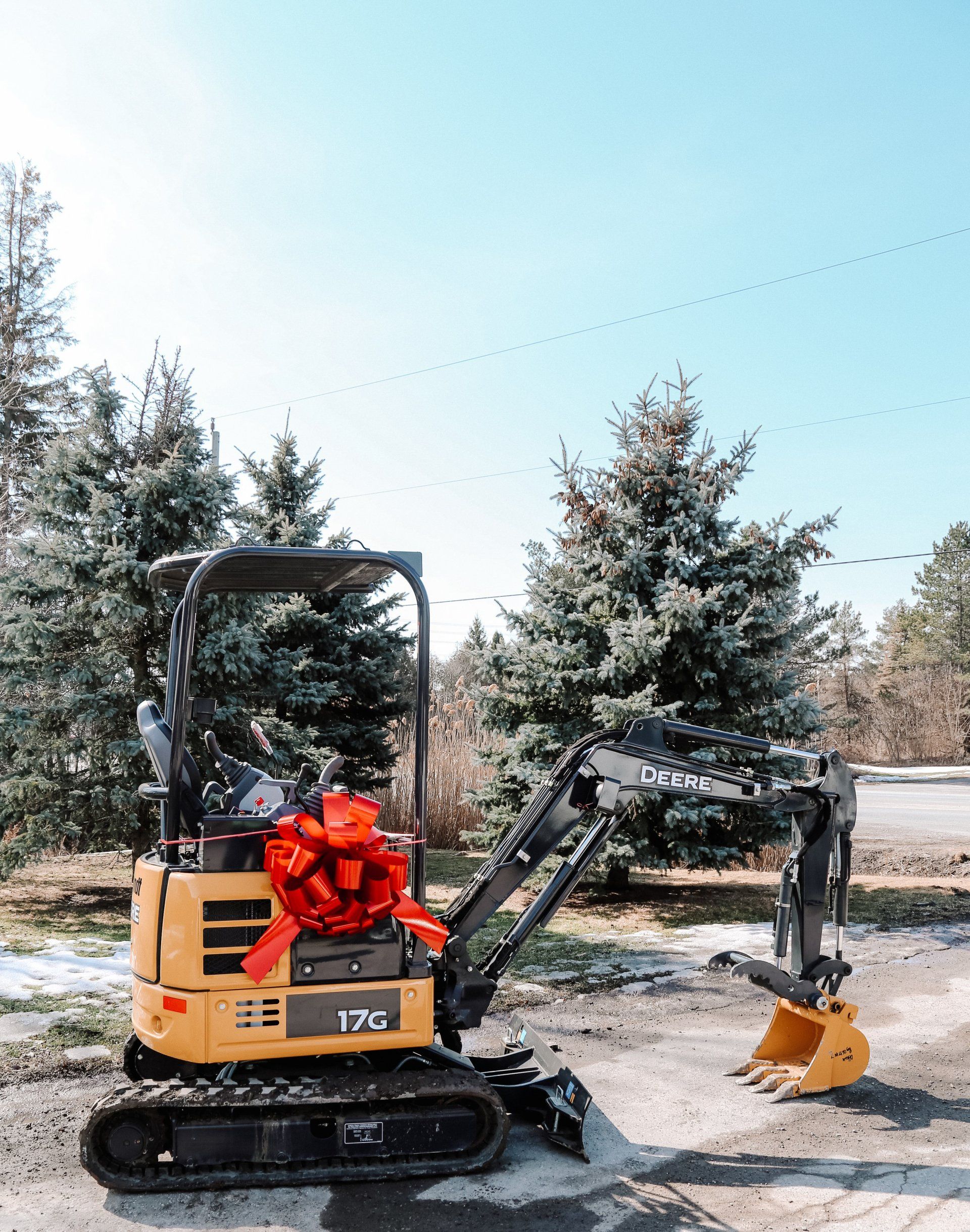 A small excavator with a red bow on it is parked on the side of the road.
