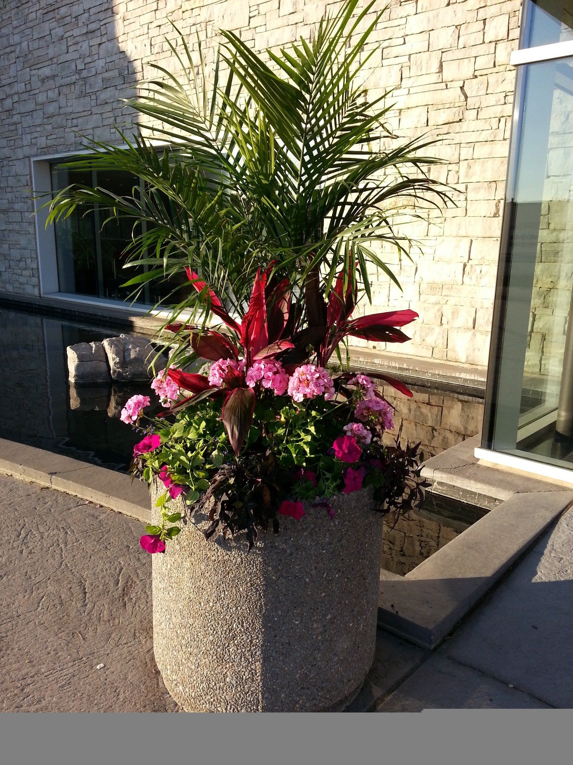 A large planter filled with flowers and plants is in front of a building.