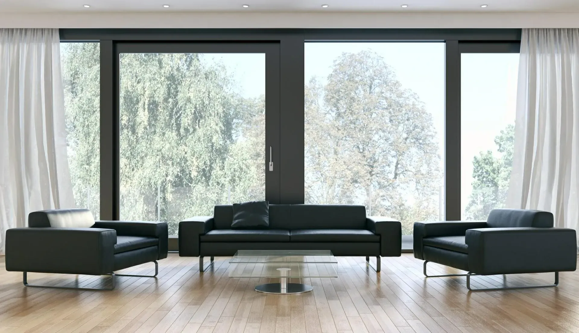 Sofá y sillones de cuero negro frente a un gran ventanal con cortinas blancas, piso de madera.