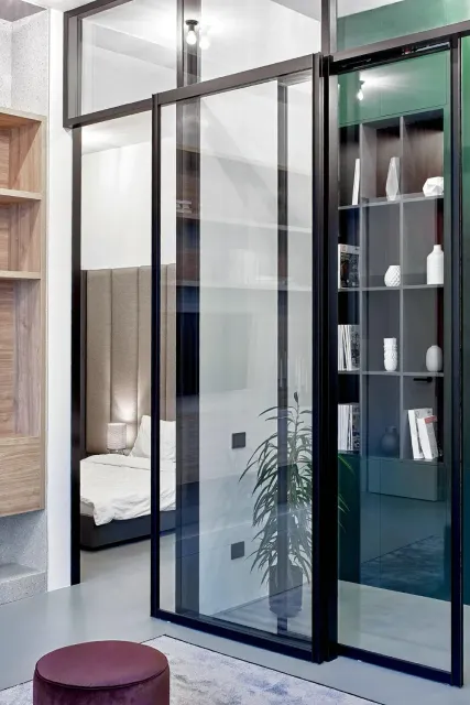 Modern interior with glass sliding doors, shelving, and bedroom visible beyond.
