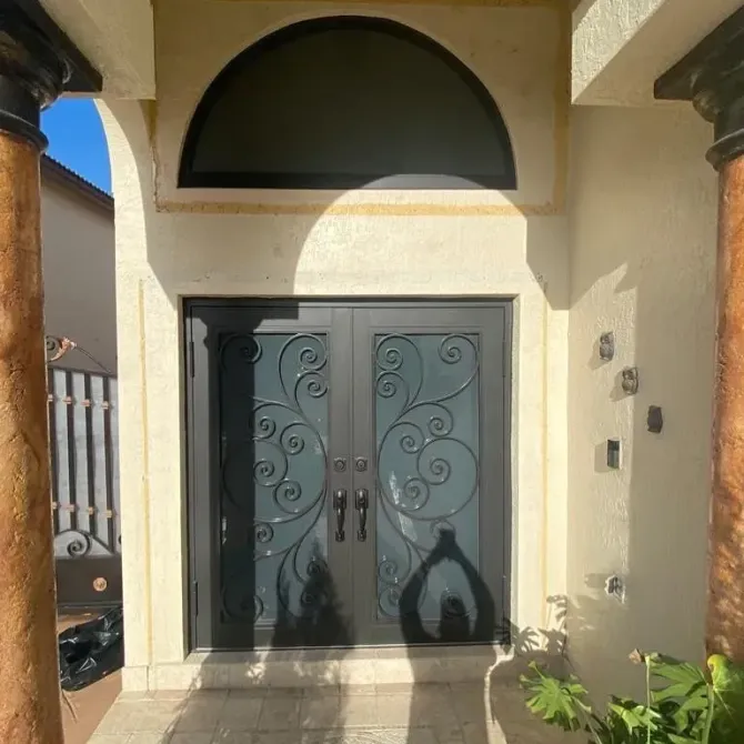 Double black ornate entry doors under a semi-circular window, between two columns.