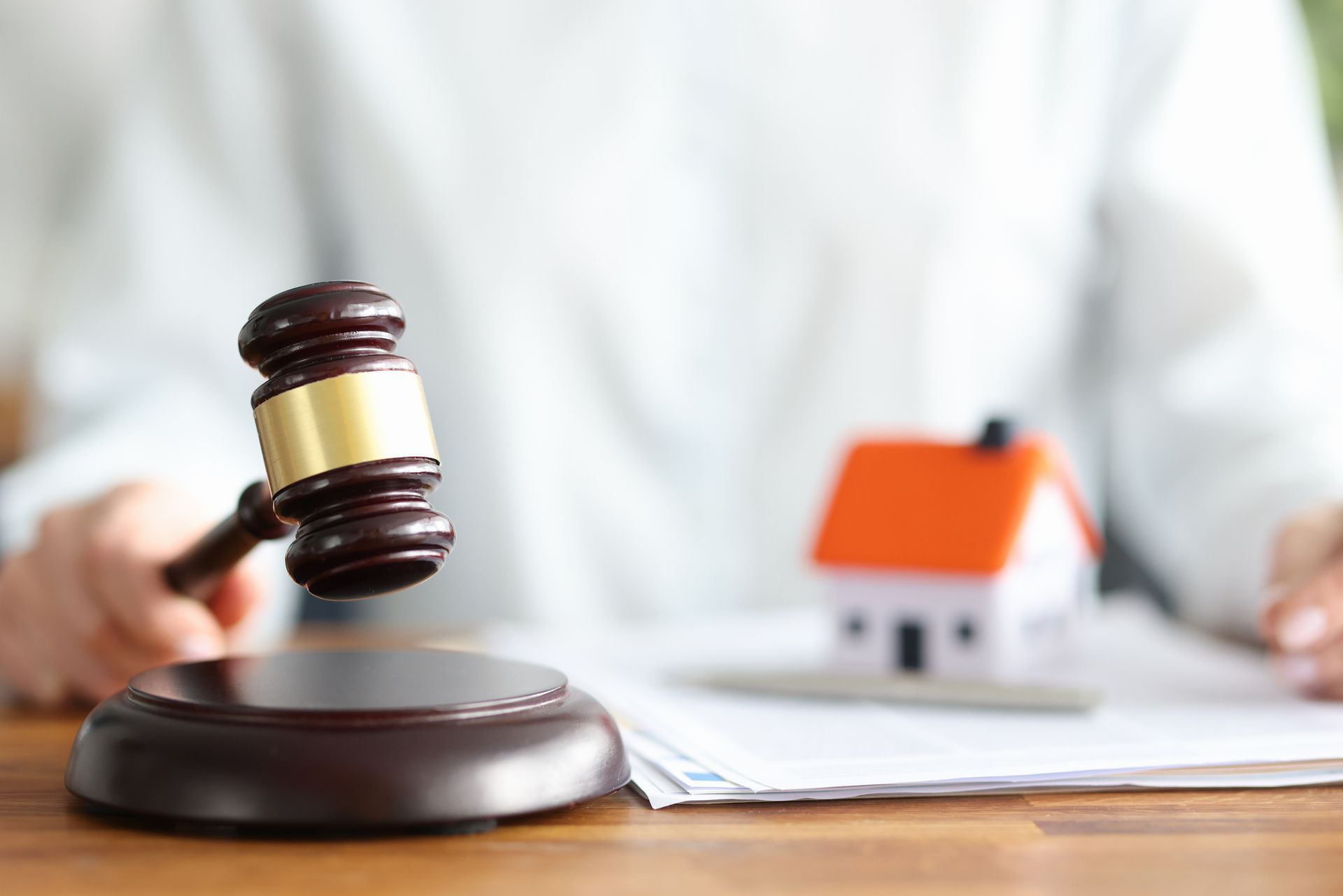 An attorney holds a wooden gavel against a background of a house and documents. An attorney holds a wooden gavel against a background of a house and documents.