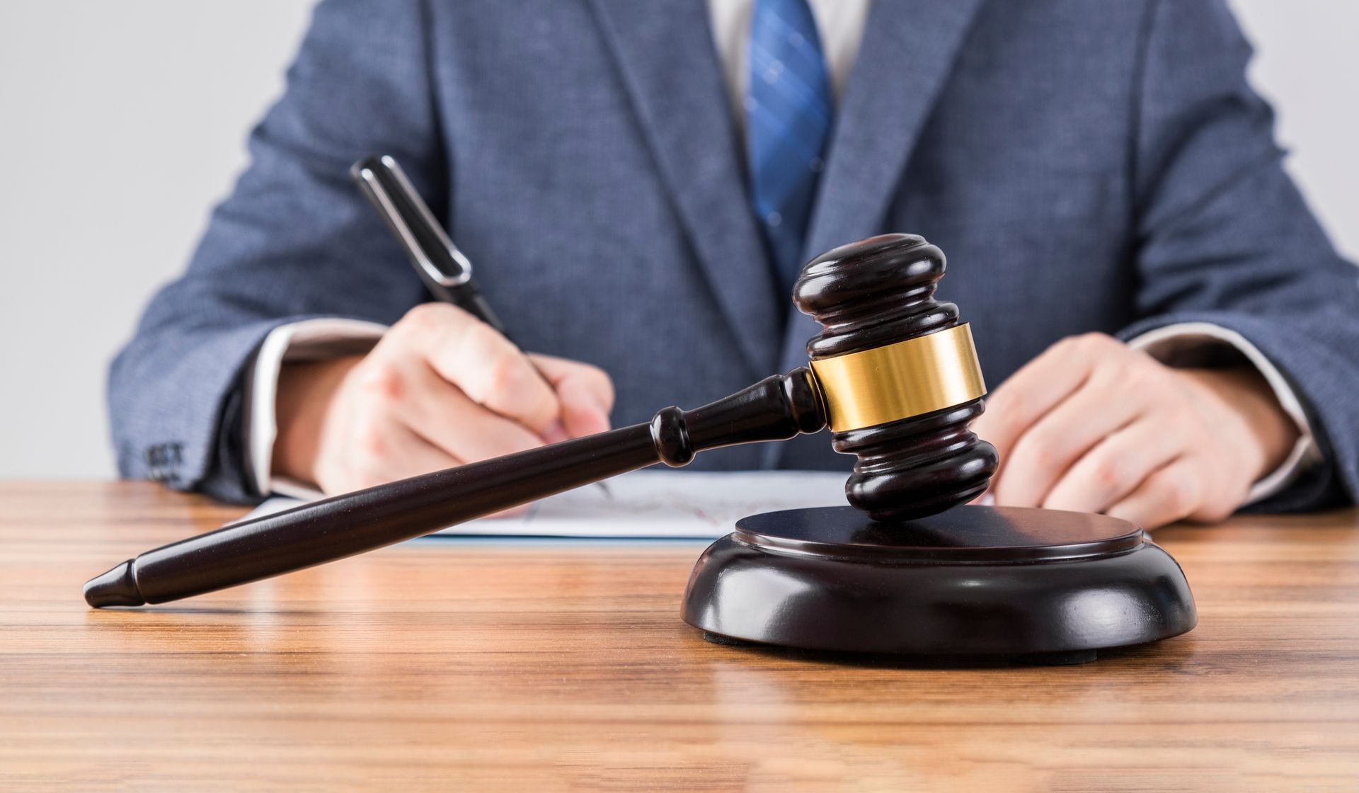 Judge in blue suit writing at desk, gavel in foreground.