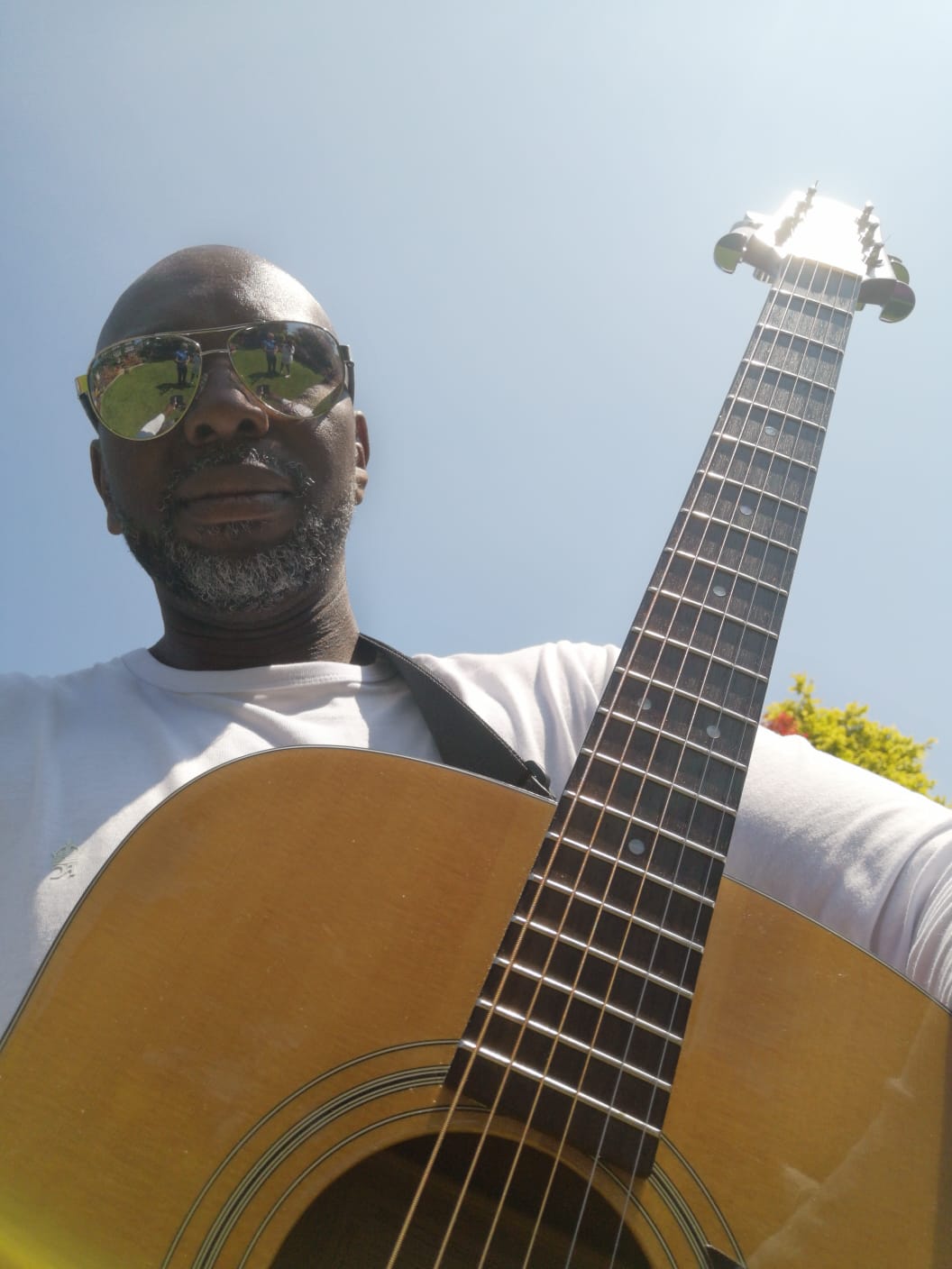 Ollie P wearing sunglasses is holding an acoustic guitar