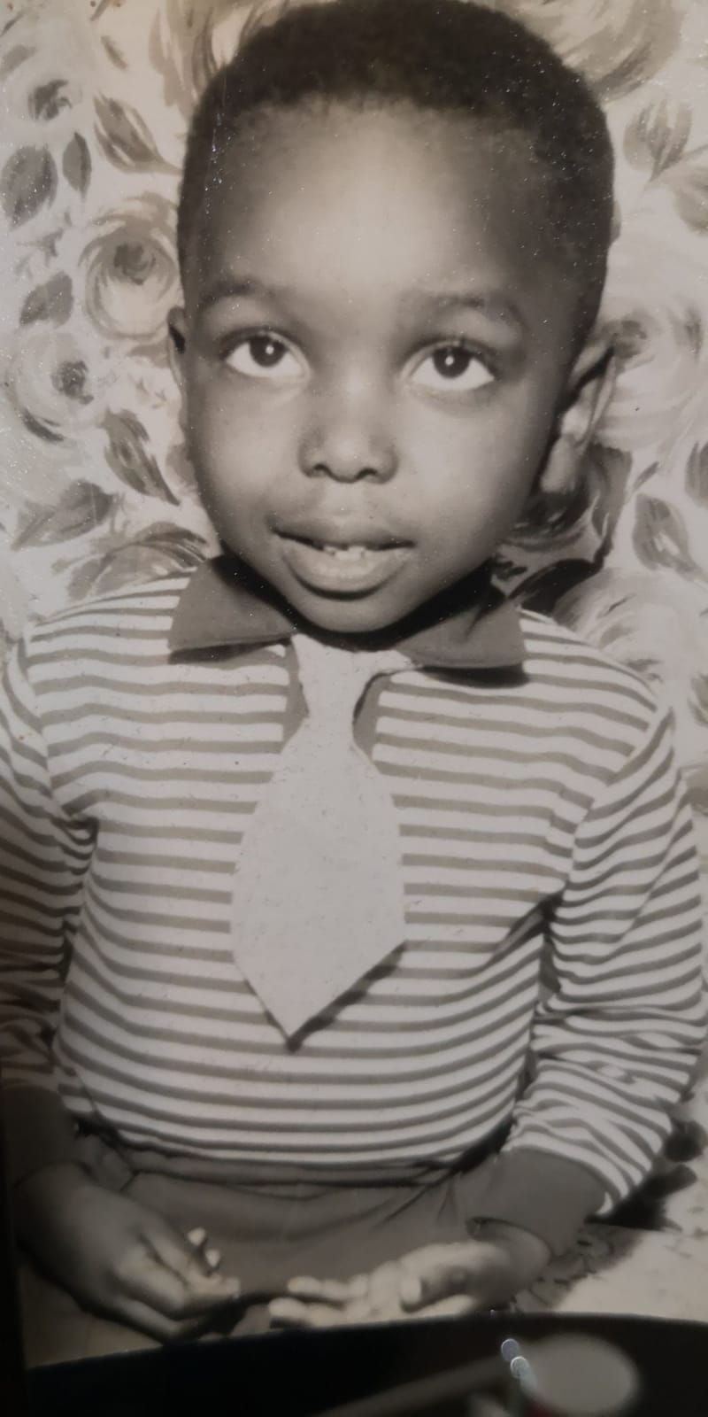 A black and white photo of a young Ollie P wearing a striped shirt and tie.