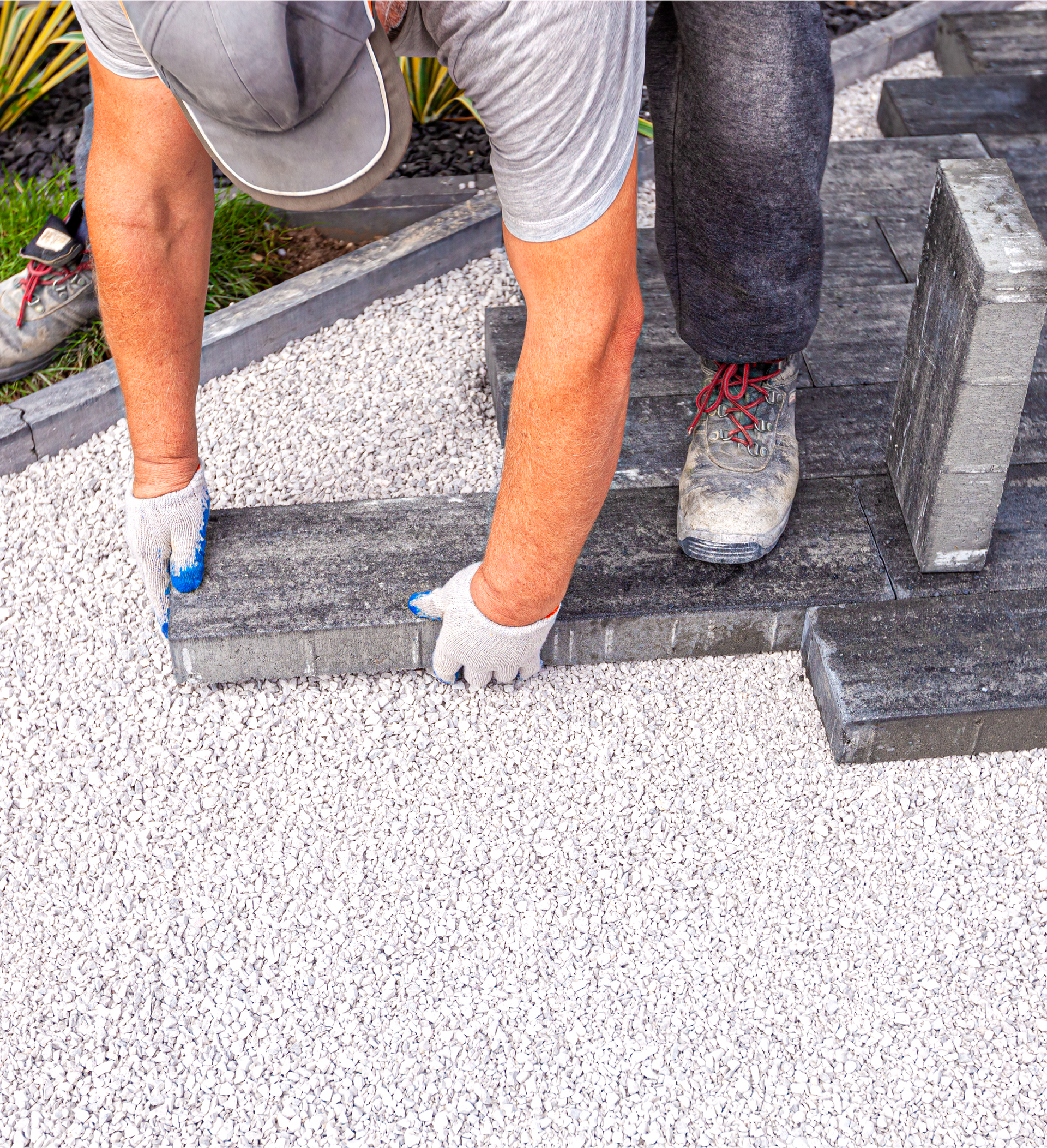 A man is laying bricks on a gravel driveway.