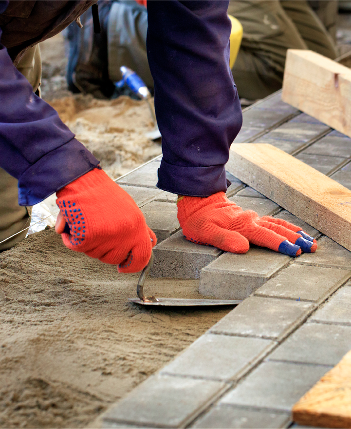 A person wearing red gloves is laying bricks on the ground