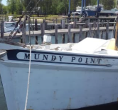 A white boat named MUNDY POINT docked at a wooden pier on a bright day.