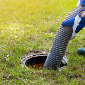 A person is pumping a hose into a septic tank.
