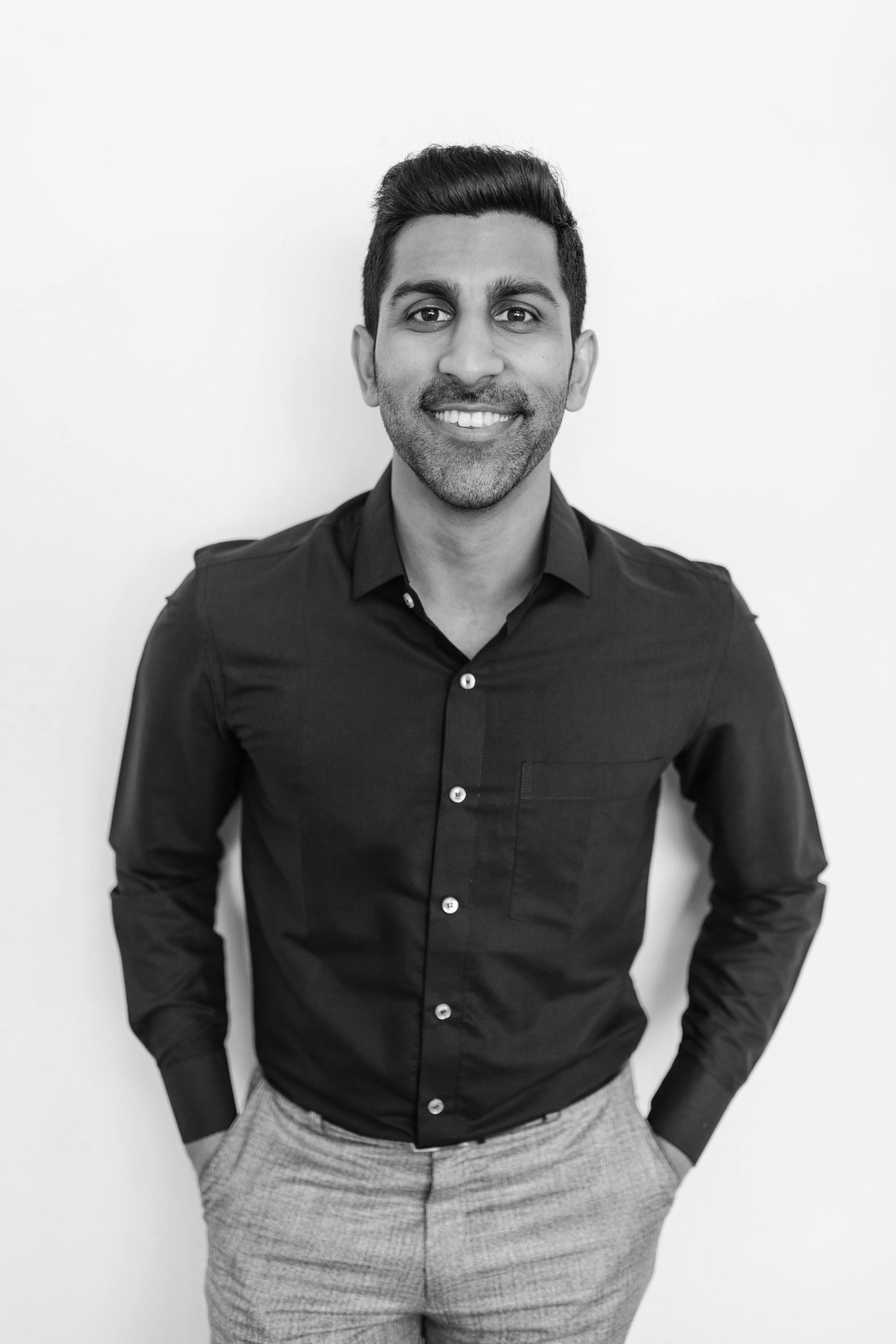 A man in a black shirt and gray pants is smiling in a black and white photo.